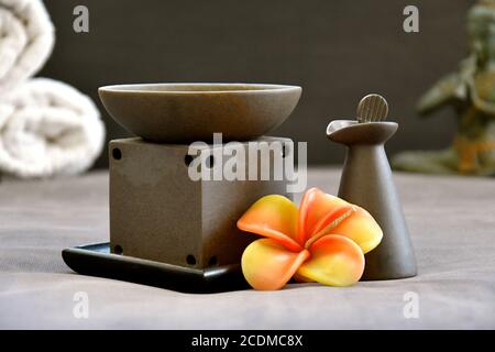 Bruciatore ad olio aromatherapy e bottiglia di argilla in una lussuosa spa ambientazione con fiori frangipani in primo piano e una meditating statua di buddha nella ba Foto Stock