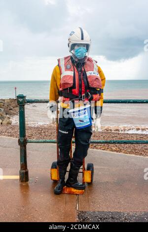 Un manichino vestito con attrezzatura di sicurezza per imbarcazioni di salvataggio RNLI, fissato a un carrello manuale, viene sostenuto contro le ringhiere per raccogliere donazioni a Sidmouth, Regno Unito Foto Stock