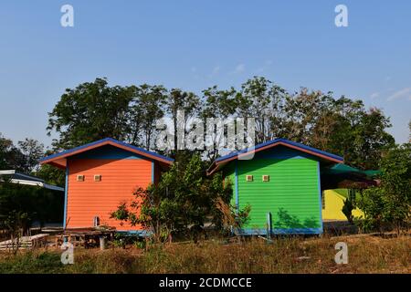 Due piccole cabine rustiche in legno colorate dipinte in arancione e verde luminoso in un ambiente rurale nel sud-est asiatico. Foto Stock