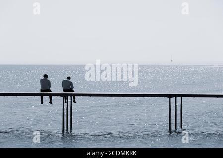 Due uomini seduti su un molo di balneazione vicino al mare, Uendelige Bro, Infinite Bridge, Aarhus, Jutland, Danimarca Foto Stock