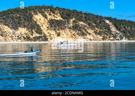 Piccola barca che si snoda lungo la costa occidentale dell'isola di Fraser con dune colorate sullo sfondo Foto Stock