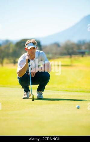 metà anni venti golfer maschio che pianifica la sua messa ha sparato al puntate su un verde in una giornata di sole Foto Stock