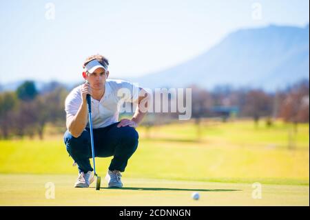 metà anni venti golfer maschio che pianifica la sua messa ha sparato al puntate su un verde in una giornata di sole Foto Stock