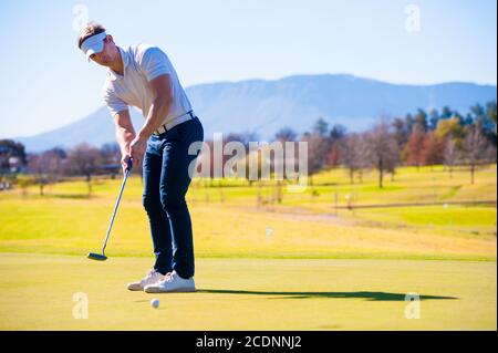 metà anni venti golfer maschio che pianifica la sua messa ha sparato al puntate su un verde in una giornata di sole Foto Stock