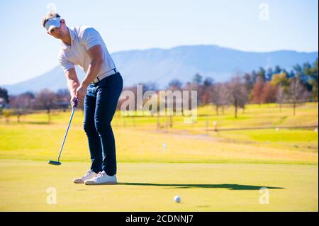 metà anni venti golfer maschio che pianifica la sua messa ha sparato al puntate su un verde in una giornata di sole Foto Stock