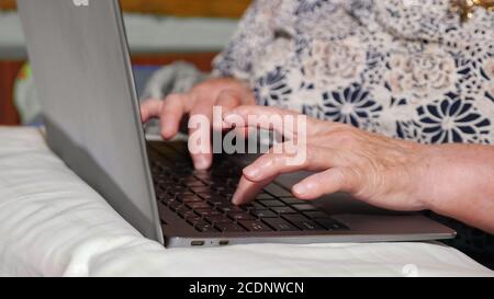 Primo piano delle mani di una donna anziana che scrive su un computer portatile. Foto Stock