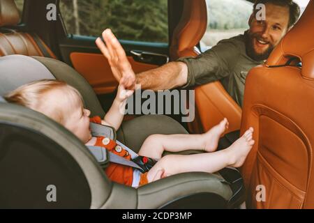 Padre con bambino in auto su strada viaggio alto cinque le mani del bambino che siede nel sedile di sicurezza uomo guida vacanza di famiglia stile di vita di viaggio felici emozioni positive Foto Stock