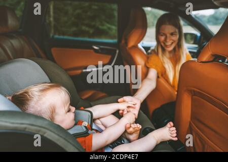 Bambino di famiglia in automobile che tiene il bambino della mano della madre seduto dentro sedile di sicurezza mamma conducente su strada viaggio vacanza stile di vita genitore con figlia in automatico Foto Stock