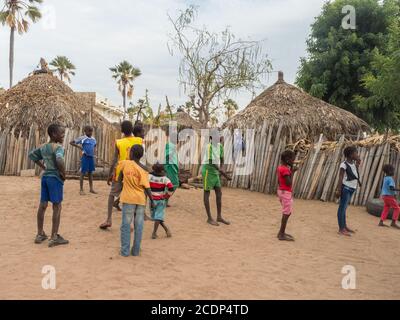 Senegal, Africa - Gennaio 2019: Gruppo di bambini nel piccolo villaggio africano tradizionale con case in argilla ricoperte di foglie di palma Foto Stock