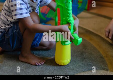 Un ragazzo da corsa misto gioca con una macchina giocattolo all'interno. Bambino prescolare con colorato giocattolo di plastica sul tappeto. Vita felice. Messa a fuoco selettiva. Foto Stock