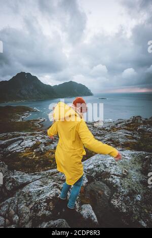 Donna in impermeabile gialla che cammina in Norvegia montagne vacanze attive Avventura all'aperto sano stile di vita ragazza da sola esplorando le isole Lofoten ventose r Foto Stock