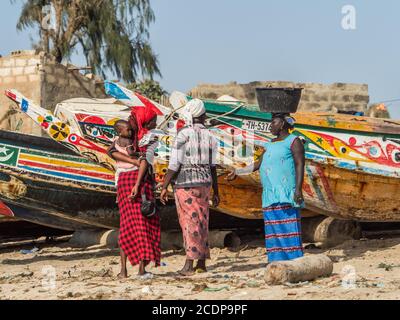 Nianing, Senegal - 24 gennaio 2019: Donna senegalese e la chiocciera sullo sfondo di colorate barche da pesca in legno in piedi sulla spiaggia di sabbia in Senegal. Foto Stock