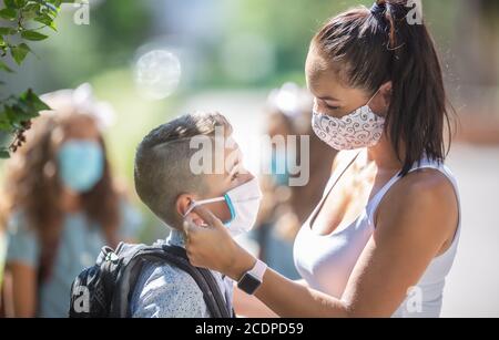 Una madre e suo figlio usano una maschera protettiva quando tornano a scuola durante la quarantena COVID-19. Foto Stock