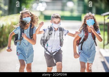 Gli studenti felici con maschere facciali corrono dalla gioia di tornare a scuola durante la quarantena Covid-19. Foto Stock