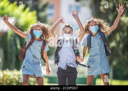 Studenti felici con maschere facciali saltano dalla gioia per tornare a scuola durante la quarantena Covid-19. Foto Stock