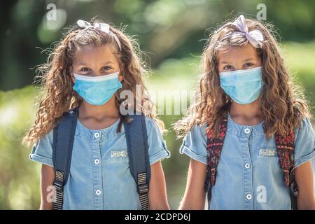 Le sorelle gemelle con maschere facciali tornano a scuola durante la quarantena Covid-19. Foto Stock