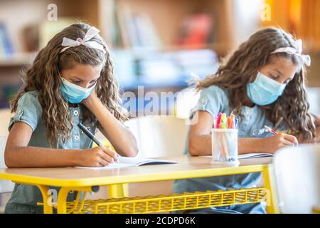 Sorelle gemelle con maschera di protezione a scuola durante la quarantena COVID-19. Foto Stock