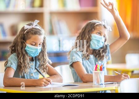 Sorelle gemelle con maschera di protezione a scuola durante la quarantena COVID-19. Foto Stock