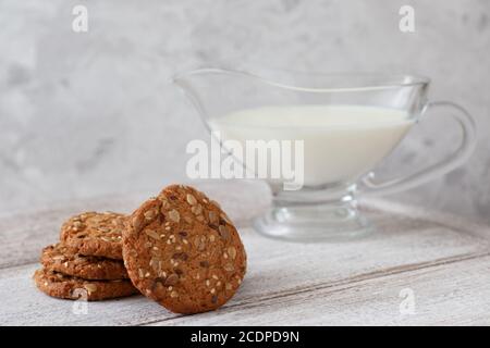 una pila di biscotti d'avena, una caraffa di latte, cereali su un tavolo di legno e uno sfondo grigio in un tasto alto. Foto Stock