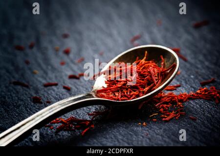 Lo zafferano in un cucchiaio su uno sfondo scuro, il fuoco selettivo, macro shot, profondità di campo Foto Stock