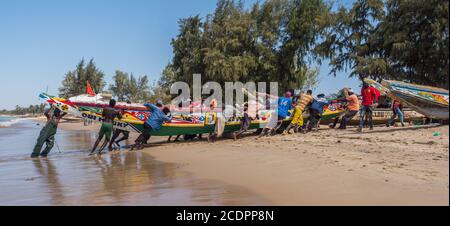 Nianing, Senegal - Gennaio 2, 2019: i pescatori la raccolta di pesce di legno colorato barca fisher permanente sulla spiaggia. Africa Foto Stock