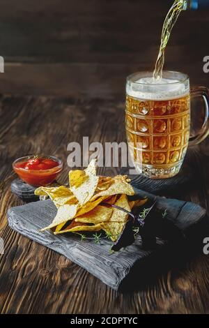 nachos su sfondo di legno con una tazza di birra. La birra si versa nella tazza. Spazio di copia Foto Stock