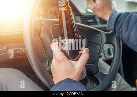 Un ubriaco alla guida di una vettura con una bottiglia di alcool in mano.Un uomo detiene una ruota motrice e una bottiglia di birra. Foto Stock