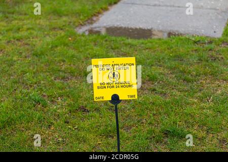 Un piccolo segno giallo è posto sul prato anteriore Agter pesticida chimico è stato applicato come un avvertimento a Non entrare. Foto Stock