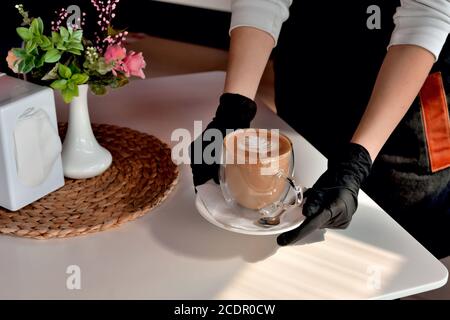 mani di una cameriera in guanti medici con una tazza da caffè, in un bar, virus, pandemia di sicurezza medica primo piano Foto Stock