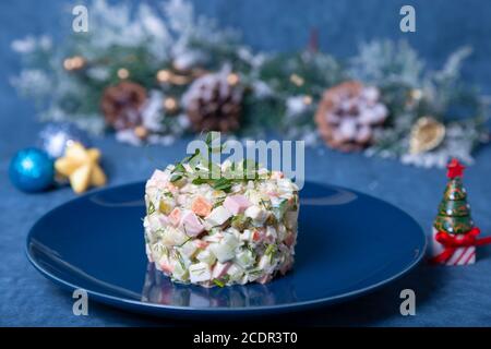 Insalata Olivier su piatto blu, decorata con germogli di piselli. Tradizionale insalata russa di Capodanno e Natale. Foto Stock