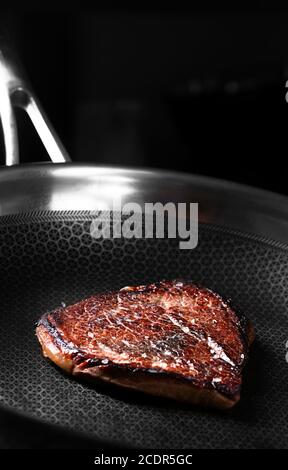 Pezzo di bistecca di manzo che si prepara sulla padella scura con olio Foto Stock