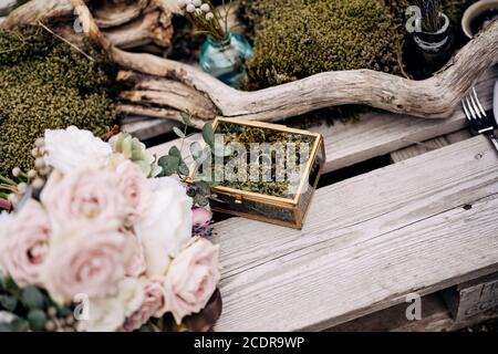 Due abiti da sposa con una scatola di gioielli a specchio su tavole di legno con un bouquet di rose rosa e driftwood. Foto Stock