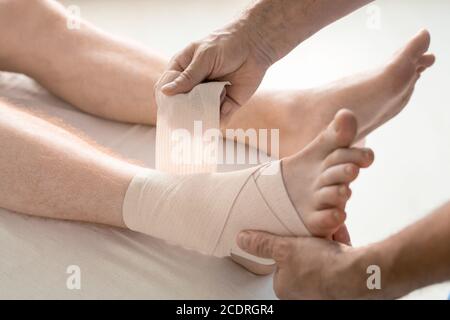 Mani di medico di riabilitazione che avvolge il piede e la caviglia dell'uomo con bendaggio Foto Stock