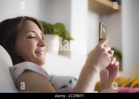 Giovane donna che usa il telefono cellulare a casa sorridendo Foto Stock