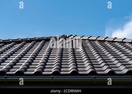 Il tetto di una casa singola coperta con una nuova piastrella ceramica in antracite contro il cielo blu, piastrelle di ventilazione in ceramica visibile sul tetto. Foto Stock