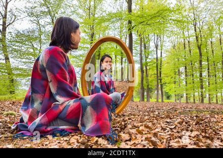 La donna si siede con lo specchio nella foresta durante la primavera Foto Stock