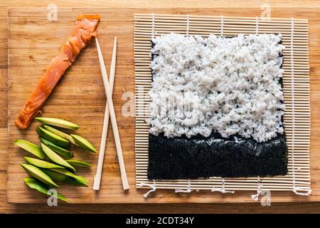 La preparazione del sushi. Salmone, avocado, il riso e le bacchette sul tavolo di legno. Foto Stock