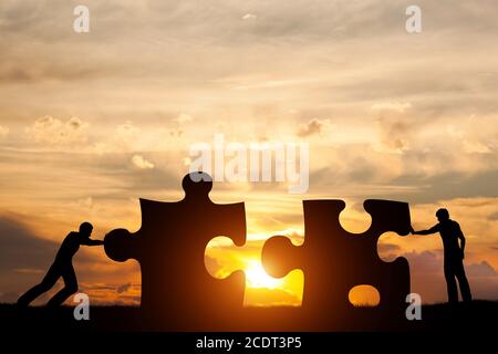 Due uomini collegano due pezzi di puzzle. Concetto di soluzione aziendale, risoluzione di un problema. Foto Stock