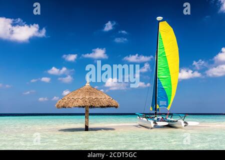 Catamarano su isola tropicale di sabbia con ombrellone, Maldive. Oceano Indiano Foto Stock