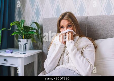 La giovane donna soffre di influenza a casa. La femmina soffia il naso tenendo il fazzoletto del tessuto, avendo sintomi di sinusite cronica, allergia stagionale Foto Stock