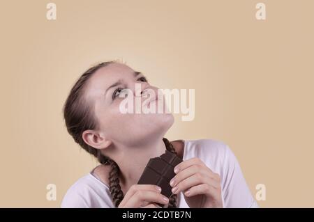 La ragazza ha un sapore di cioccolato. La ragazza sta godendo il gusto del cioccolato. Deliziatevi con il gusto del cioccolato. Giornata del cioccolato. Giorno dei dolci. La ragazza è sparata Foto Stock