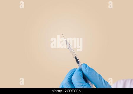 Un infermiere tiene una siringa con un'iniezione nelle mani. Infermiere in guanti medici. Preparazione per l'iniezione. Fotografato con uno sfondo giallo. Foto Stock