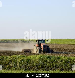 Un trattore con un aratro stabilisce il terreno. La coltivazione del suolo sul fie Foto Stock