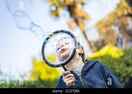 Bambino di 7 anni all'aperto nel giardino in inverno rende grandi bolle di sapone Foto Stock