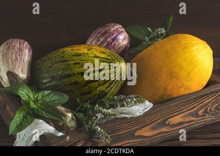 Melone, basilico, menta, melanzane di graffiti viola, cipolla e basilico fresco verde in una scatola di legno su sfondo ligneo vintage in rus Foto Stock