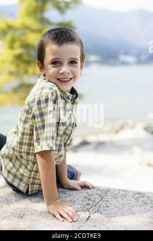 ritratto di ragazzo di 9 anni sorridente con camicia colorata seduto su una parete Foto Stock