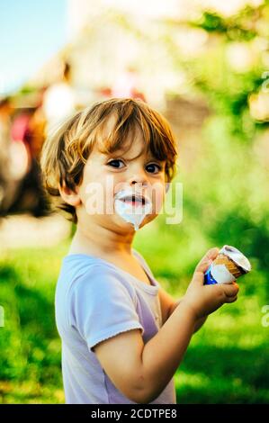 il bambino mangia il gelato in una giornata estiva nell' ombra di un albero Foto Stock