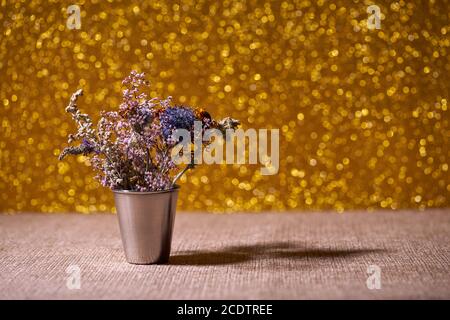 Fiori secchi in vaso metallico decorativo su sfondo giallo offuscato Foto Stock