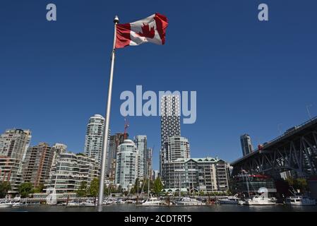 Una bandiera canadese vola di fronte agli appartamenti del centro e ai condomini sullo skyline di Vancouver, British Columbia, Canada Foto Stock