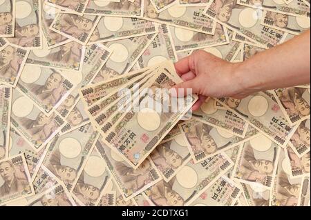 Mano che tiene cinque pezzi di 10,000 yen note - sfondo con diverse diecimila yen note (fronte). Denaro giapponese. Foto Stock